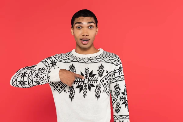 Surprised african american man in sweater with winter pattern pointing with finger at himself isolated on red — Stock Photo