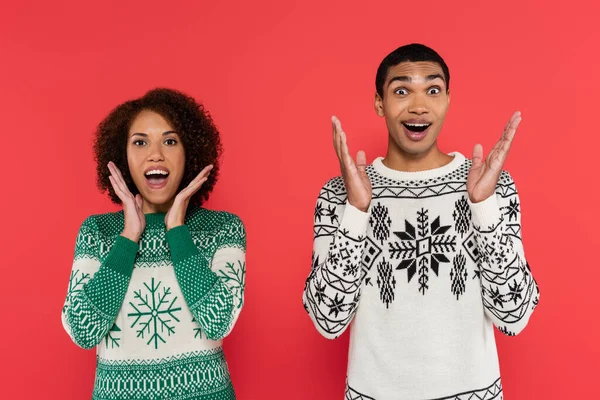 Amazed african american couple in warm sweaters looking at camera and showing wow gesture isolated on red — Stock Photo