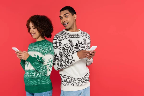 Curious african american man looking at smartphone in hands of girlfriend isolated on red — Stock Photo