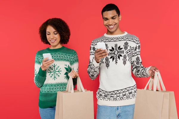 Felice coppia afro-americana con telefoni cellulari e shopping bag isolati su rosso — Foto stock