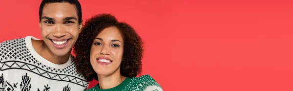 Joyeux couple afro-américain en pull d'hiver souriant à la caméra isolée sur rouge, bannière — Photo de stock