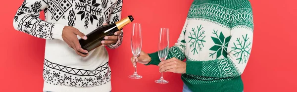 Partial view of african american woman with glasses near man pouring champagne isolated on red, banner — Stock Photo