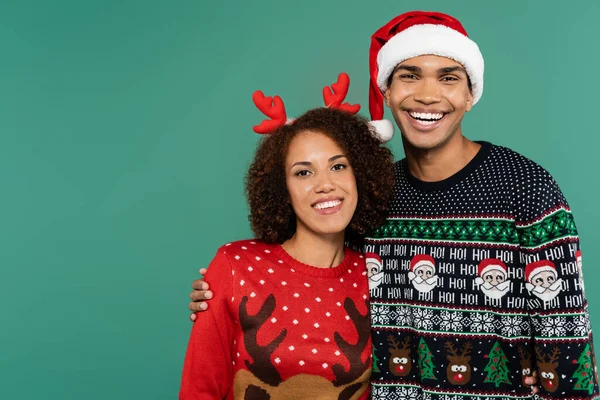 Happy african american man embracing girlfriend in reindeer horns headband isolated on green — Stock Photo