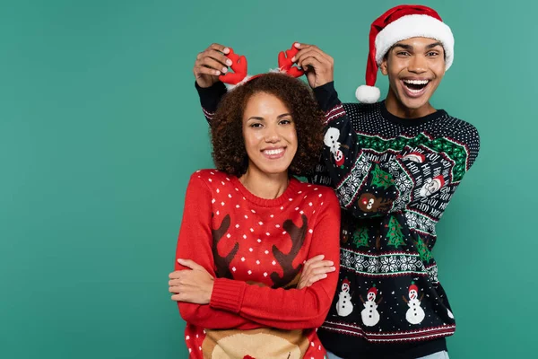 Excitado afroamericano hombre en santa hat tocando cuernos de reno en diadema de novia aislado en verde — Stock Photo