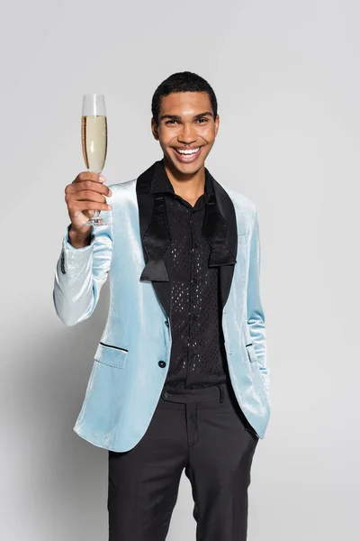 Hombre afroamericano feliz en ropa festiva elegante tostadas con champán aislado en gris - foto de stock