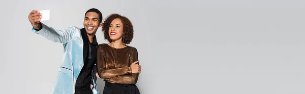 Heureux homme afro-américain dans blazer élégant prendre selfie avec jeune copine isolé sur gris, bannière — Photo de stock