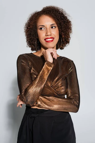 Morena afroamericana americana mujer en elegante blusa sonriendo y mirando hacia otro lado en gris — Stock Photo