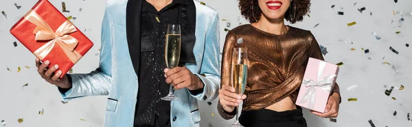 Partial view of elegant african american couple with christmas presents and champagne on grey background, banner — Stock Photo