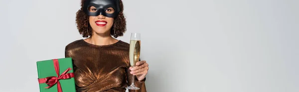 Afrikanisch-amerikanische Frau in eleganter Bluse und Hasenmaske mit Champagnerglas und Geschenkbox isoliert auf grau, Banner — Stockfoto