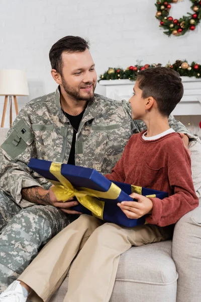 Glücklicher Militärmann mit Sohn, die einander in der Nähe geöffneter Weihnachtsgeschenkschachtel anschauen — Stockfoto