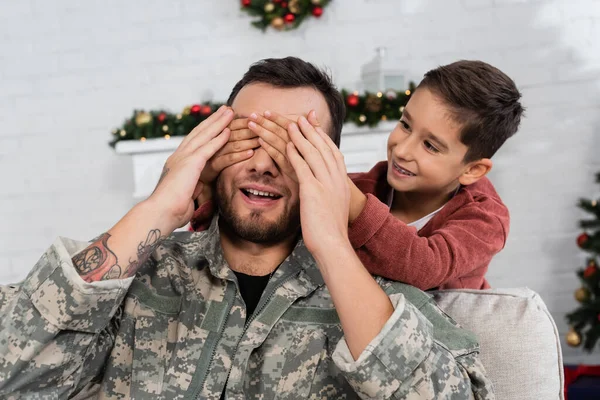 Happy kid covering eyes of smiling dad in camouflage while playing guess who game — Stock Photo