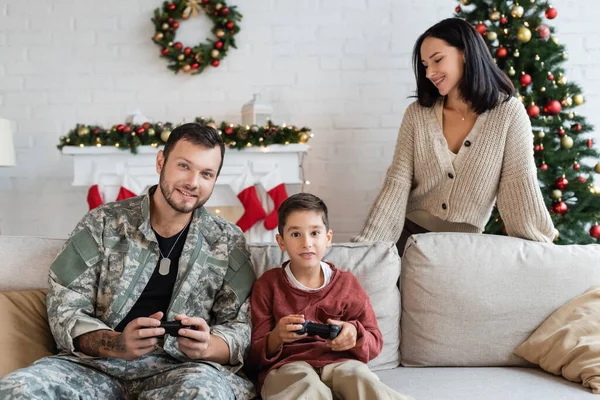 KYIV, UKRAINE - 21 SEPTEMBRE 2022 : femme heureuse regardant son fils et son mari excités dans le jeu de camouflage à la maison — Photo de stock