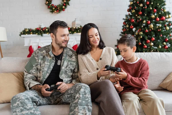 KYIV, UKRAINE - SEPTEMBER 21, 2022: smiling military man looking at wife giving joystick to son — Stock Photo