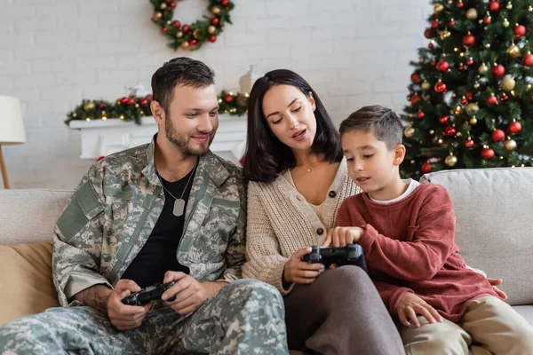 KYIV, UKRAINE - SEPTEMBER 21, 2022: boy pointing at joystick near mother and father in military uniform — Stock Photo