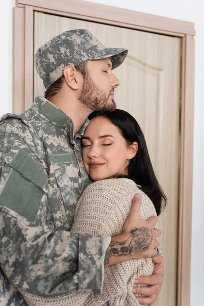 Bearded man in military uniform hugging happy wife while coming back home — Stock Photo