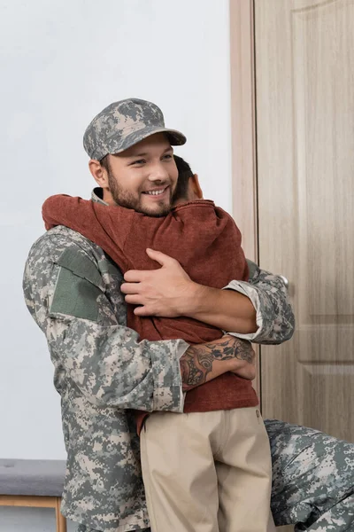 Fröhlicher Soldat umarmt Sohn, der ihn zu Hause trifft — Stockfoto