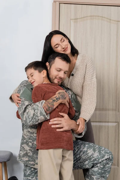 Military man with closed eyes hugging family when coming back home — Stock Photo