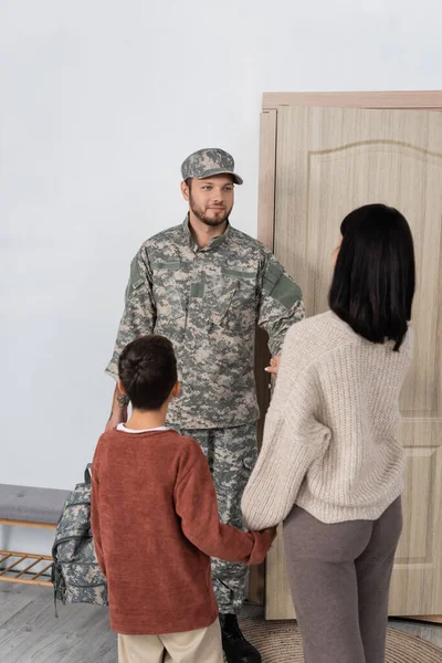 Femme avec fils rencontrer mari en camouflage près de la porte d'entrée à la maison — Photo de stock