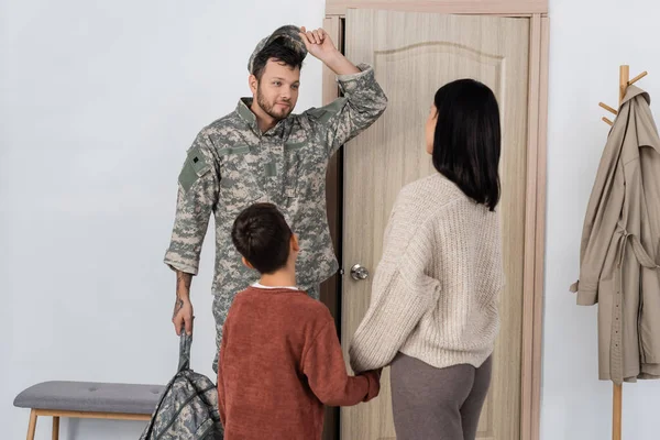 Sorrindo homem tirando o boné militar perto de esposa e filho em casa — Fotografia de Stock