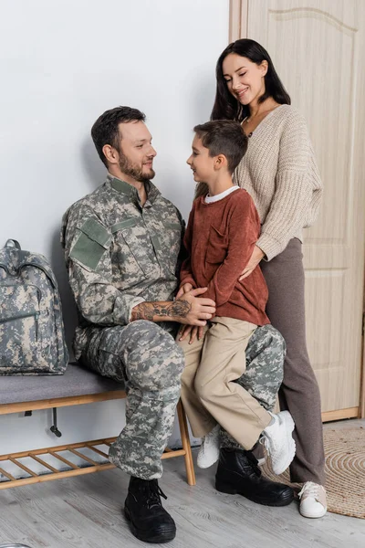 Garçon assis sur les tours de père en camouflage près de maman heureuse — Photo de stock