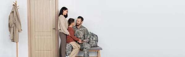 Militaire assis avec son fils près de sa femme et porte d'entrée à la maison, bannière — Photo de stock