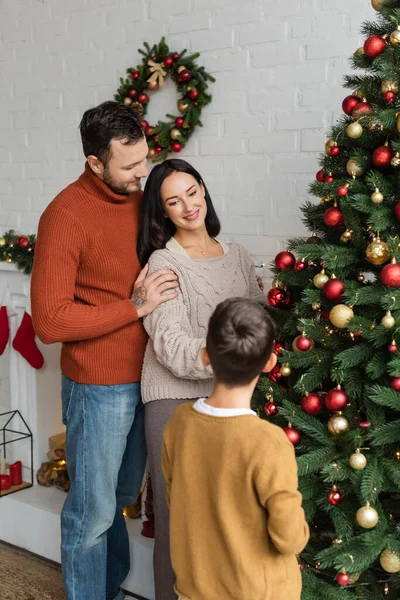 Happy man embracing wife decorating christmas tree with son at home — Stock Photo