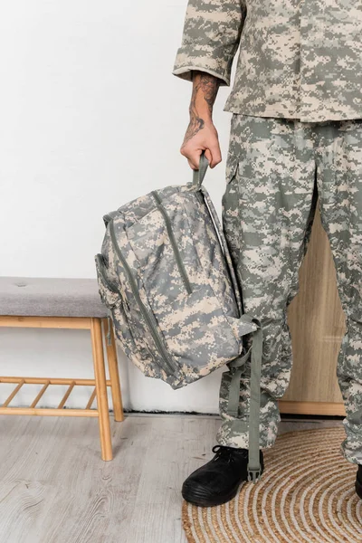 Vista cortada de homem militar em camuflagem segurando mochila quando voltar para casa — Fotografia de Stock