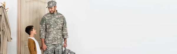 Military man with backpack holding hands with son meeting him near door at home, banner — Stock Photo