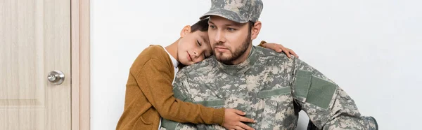 Boy with closed eyes hugging thoughtful dad in military uniform at home, banner — Stock Photo