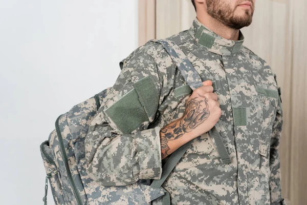 Teilbild eines bärtigen Militärangehörigen mit Tätowierung, der zu Hause einen Rucksack hält — Stockfoto