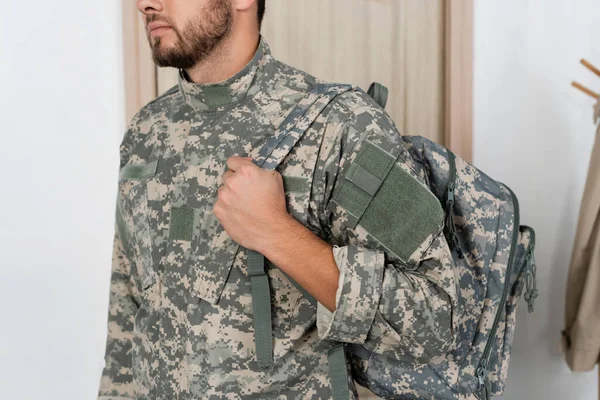 Частичный вид солдата в военной форме, стоящего с рюкзаком дома — стоковое фото