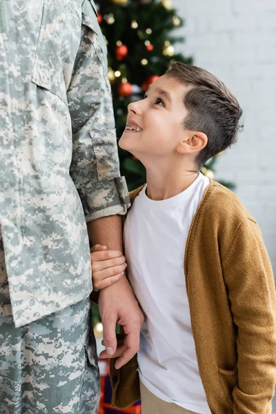 Heureux garçon regardant père en uniforme militaire et tenant sa main à la maison — Photo de stock