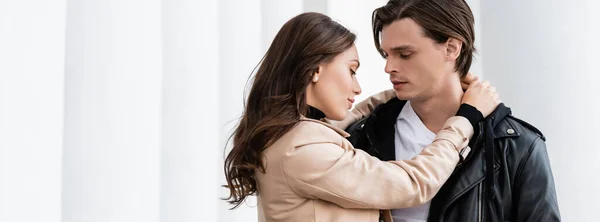 Bastante joven mujer abrazando novio en negro elegante chaqueta al aire libre, bandera - foto de stock