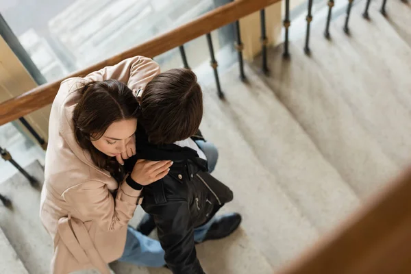 Top view of pretty woman in beige trench coat hugging young man in black jacket standing on stairs — Stock Photo