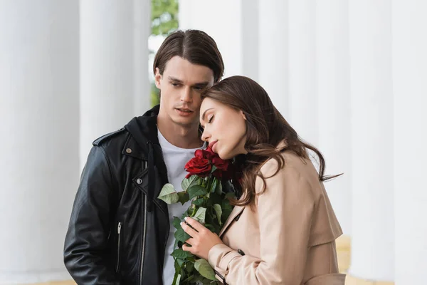 Bella giovane donna odore rose rosse vicino elegante fidanzato in giacca — Foto stock