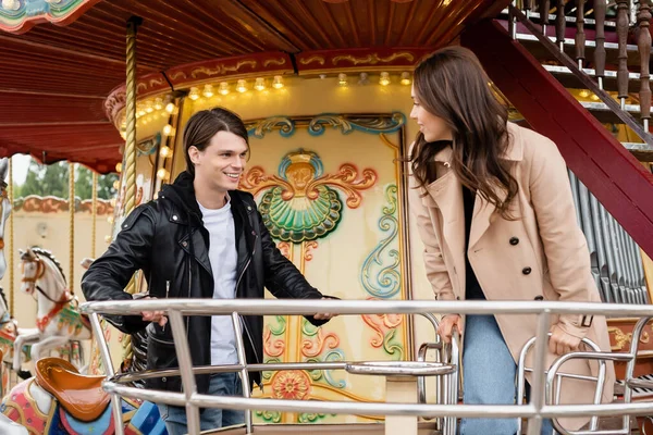 Happy couple in autumnal outfits looking at other on carousel in amusement park — Stock Photo