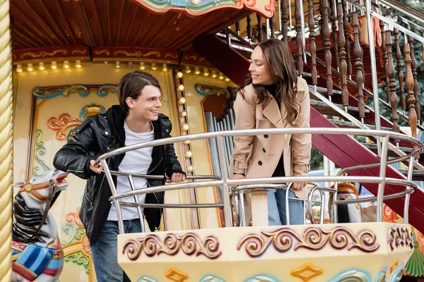 Cheerful couple in autumnal outfits looking at other on carousel in amusement park — Stock Photo