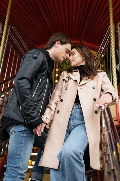 Visão de baixo ângulo de casal sensual de mãos dadas enquanto em pé no carrossel no parque de diversões — Fotografia de Stock