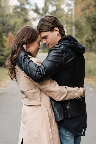 Вид збоку стильний молодий чоловік обіймає красиву дівчину в траншеї пальто на відкритому повітрі — стокове фото