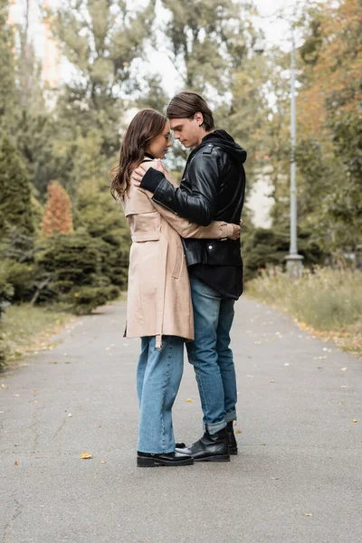 Full length view of stylish young man hugging pretty girlfriend in trench coat outdoors — Stock Photo