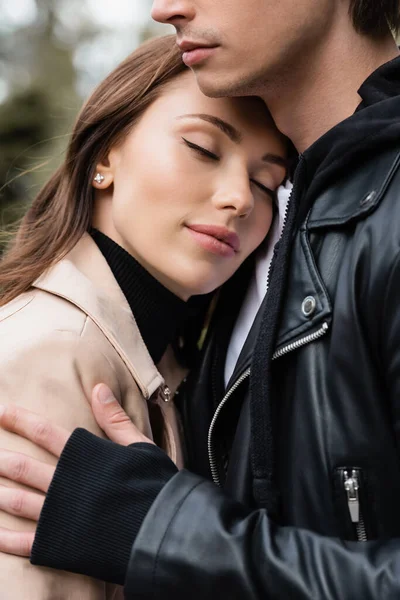 Pretty young woman with closed eyes leaning on chest of boyfriend in black jacket — Stock Photo