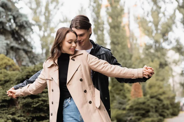 Cheerful man holding hands with pleased girlfriend in beige trench coat — Stock Photo