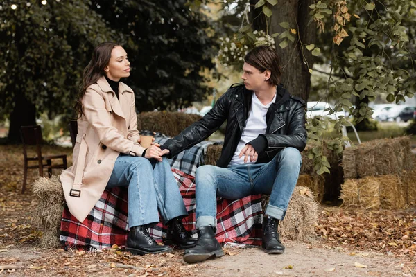 Stilvoller Mann hält Hand seiner Freundin, die mit Pappbecher auf karierter Decke sitzt — Stockfoto