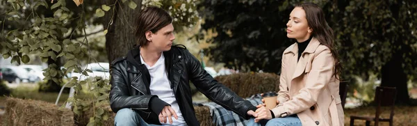 Homme élégant tenant la main de la petite amie assise avec tasse en papier dans le parc, bannière — Photo de stock