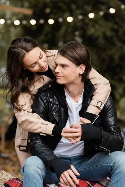 Smiling young woman in trench coat hugging stylish boyfriend in park — Stock Photo