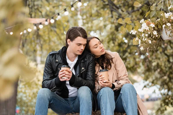 Young woman with closed eyes holding paper cup and leaning on shoulder of boyfriend — Stock Photo