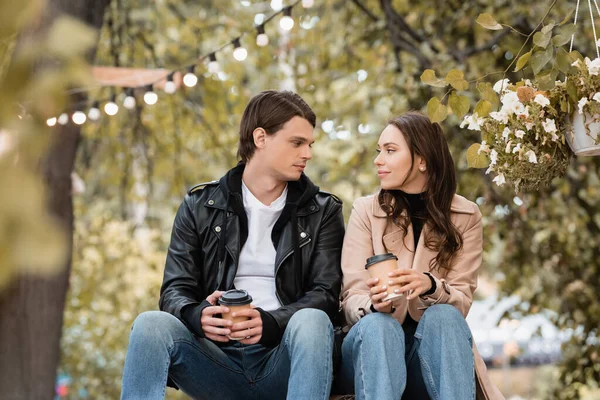 Young woman and man in stylish outfits holding paper cups and looking at each other — Stock Photo