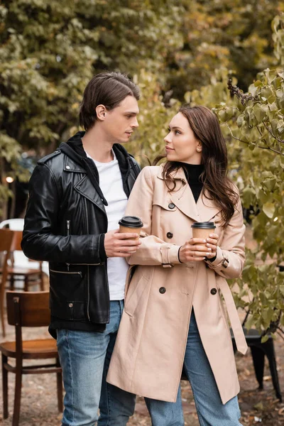 Young woman and man in stylish outfits holding coffee to go and looking at each other — Stock Photo