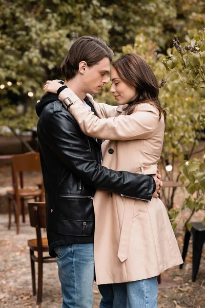 Vue latérale du couple avec les yeux fermés debout dans des tenues élégantes et câlins dans le parc automnal — Photo de stock