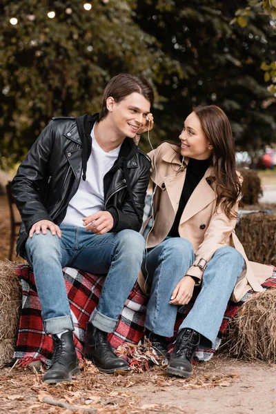 Cheerful young woman adjusting wired earphone in ear of happy boyfriend — Stock Photo